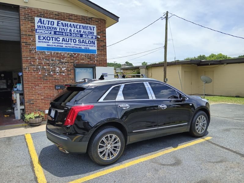 A black car is parked in a parking lot in front of a brick building.
