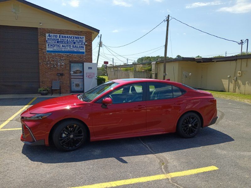 A red car is parked in a parking lot in front of a building.