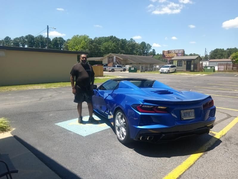 A man is standing next to a blue sports car in a parking lot