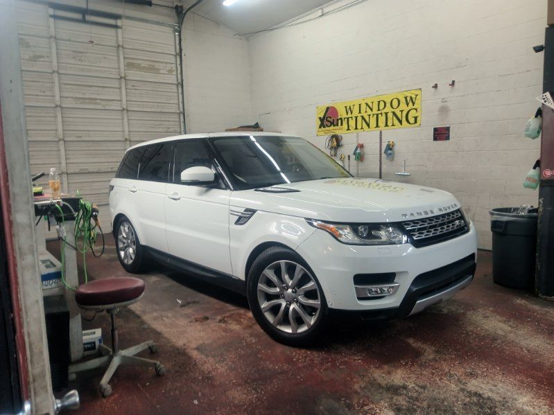 A white range rover sport is parked in a garage next to a window tinting sign.