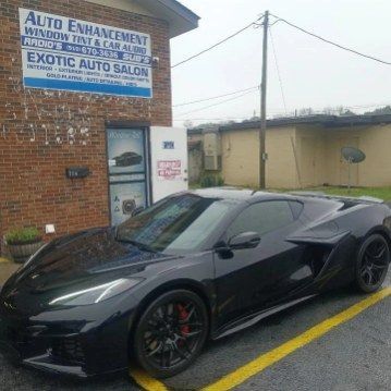 A black sports car is parked in front of a brick building.