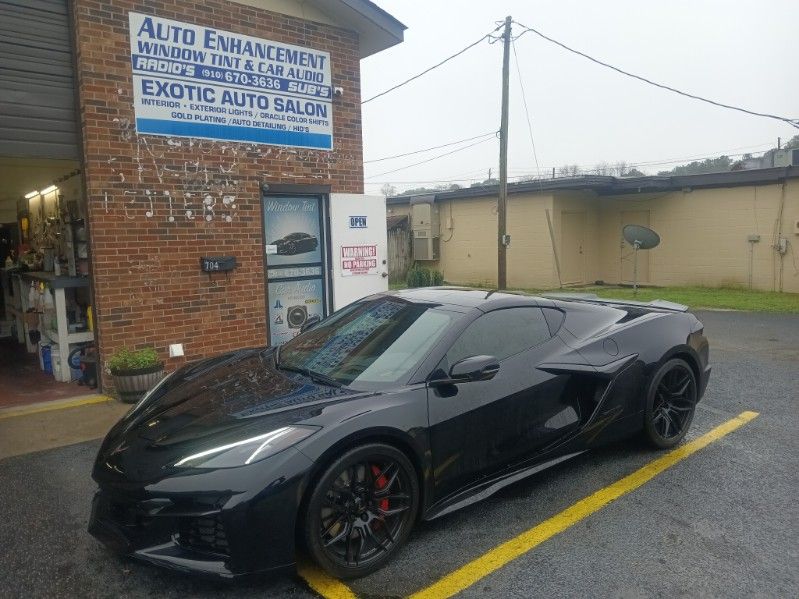 A black sports car is parked in a parking lot in front of a brick building.