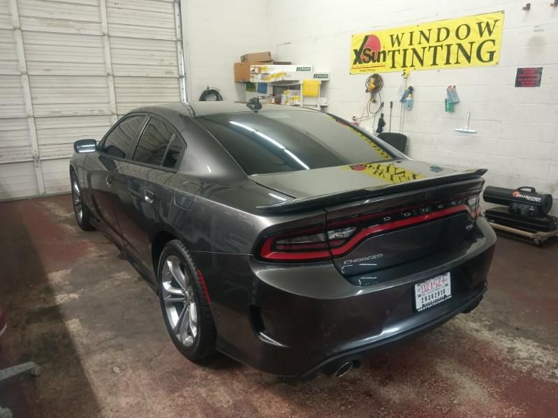 A gray dodge charger is parked in a garage next to a window tinting sign.