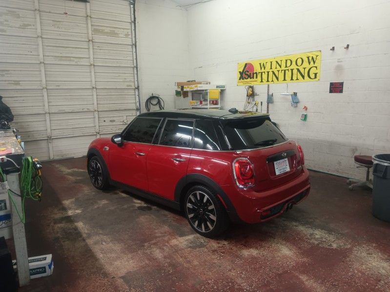 A red mini cooper is parked in a garage under a sign that says window tinting.