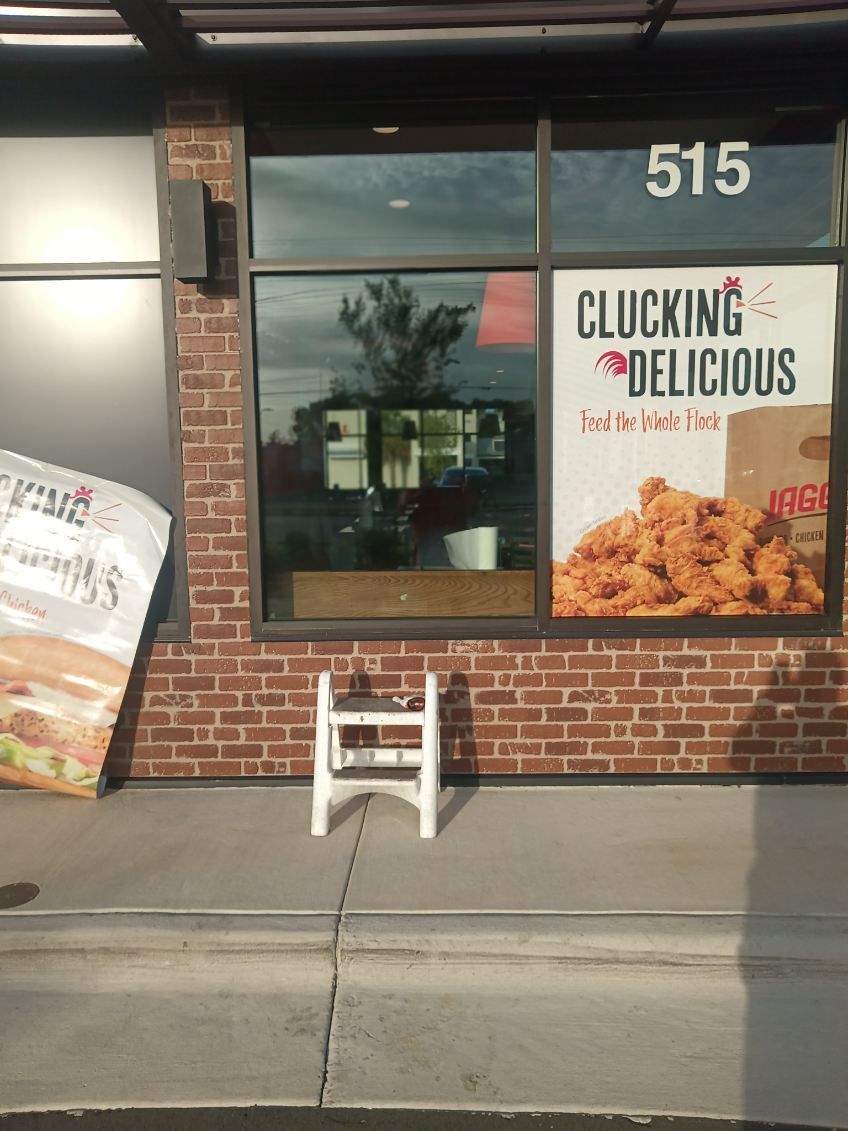 A stool is sitting on the sidewalk in front of a fast food restaurant.