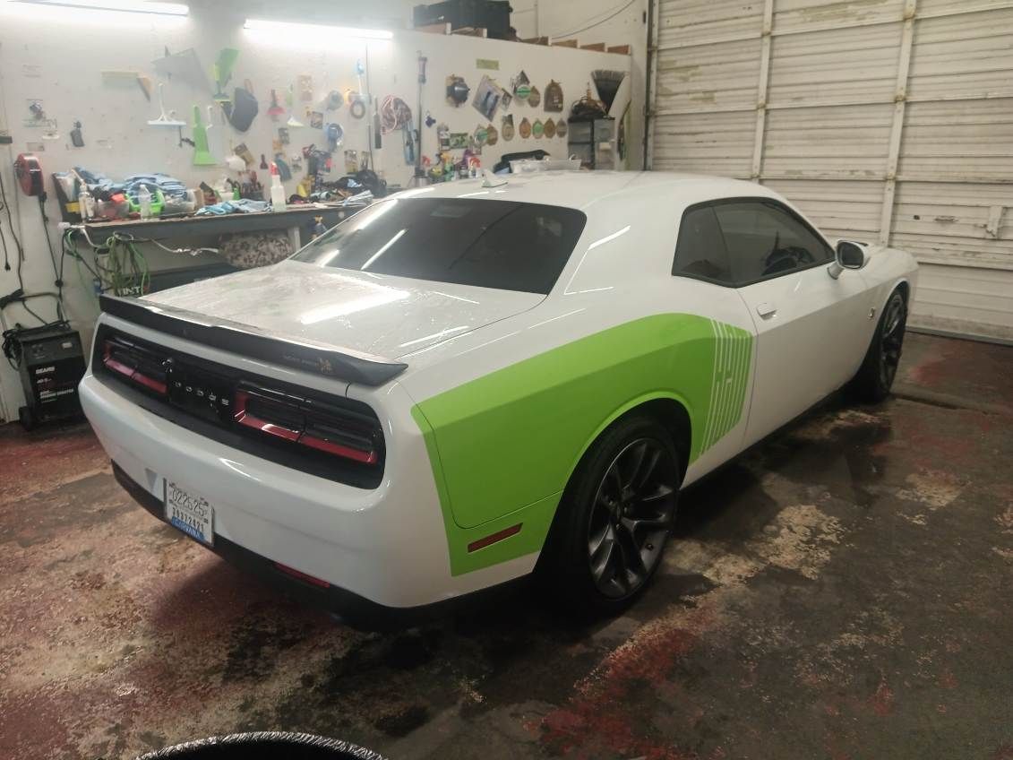 A white dodge challenger with green stripes is parked in a garage.