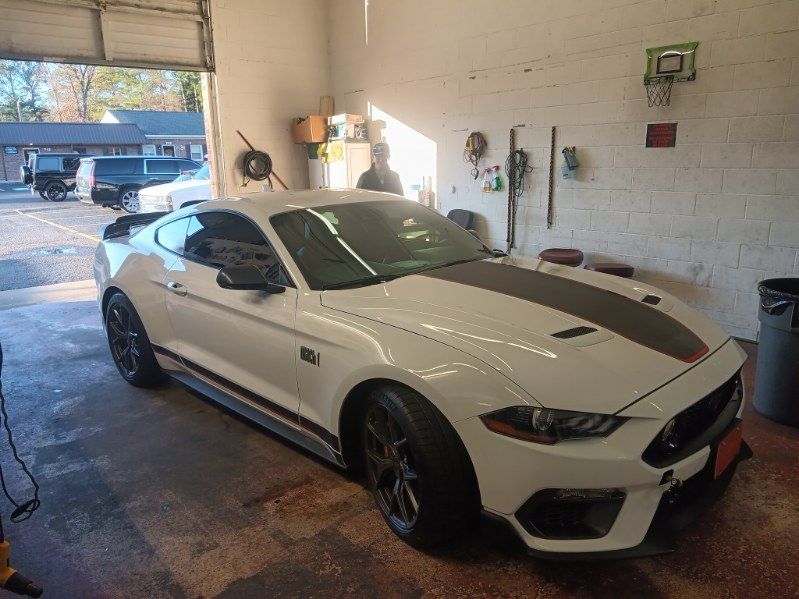 A white mustang is parked in a garage next to a garage door.