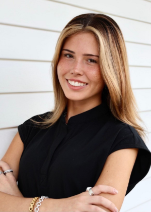 Woman with blonde highlights smiles, arms crossed, in front of a white, slatted wall.