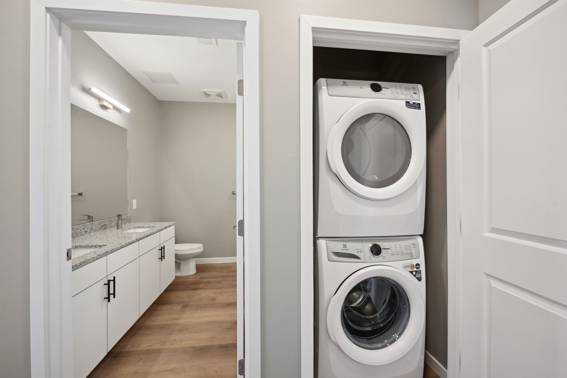 A laundry closet with stacked white washer and dryer units next to an open doorway leading into a modern bathroom.