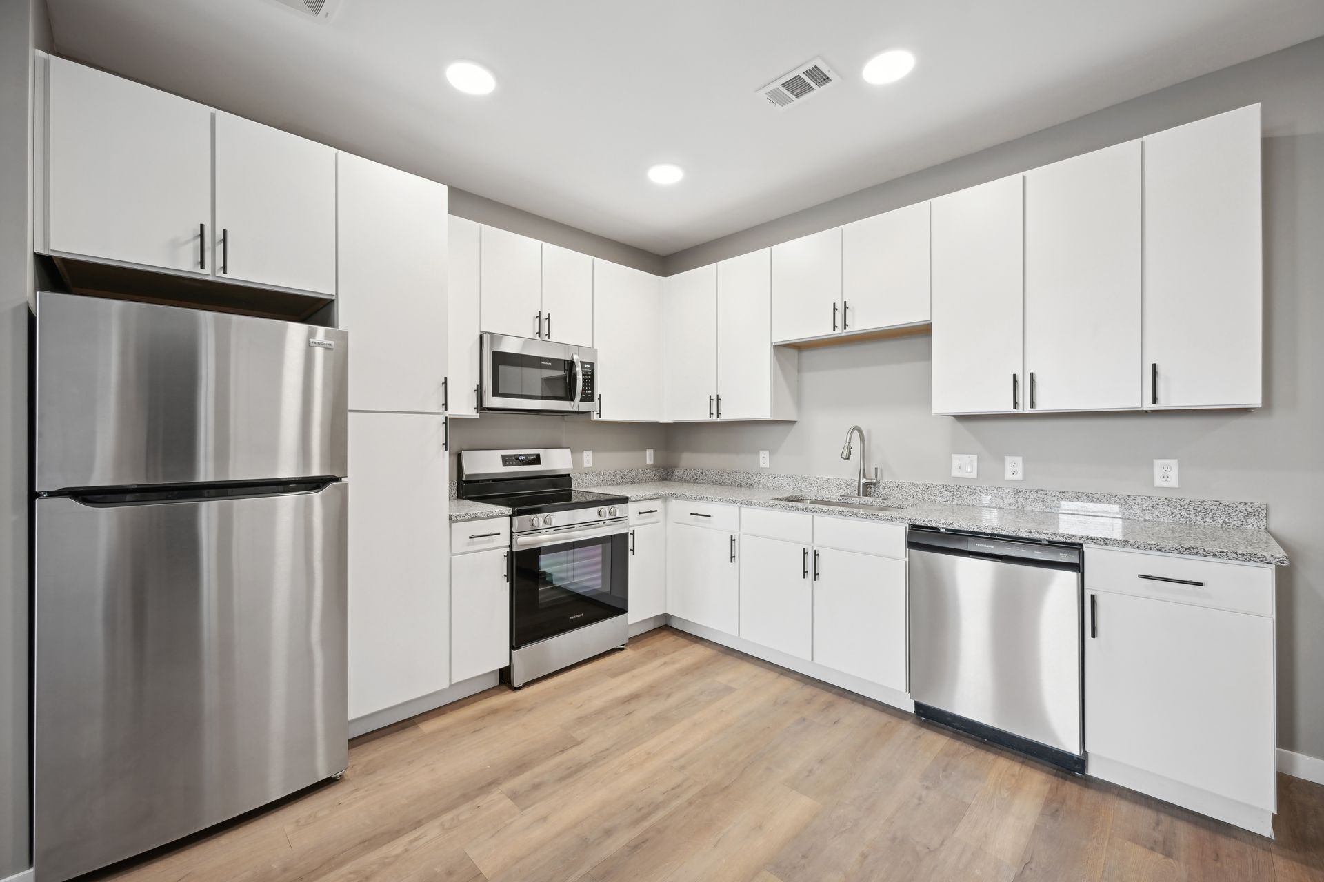 Modern kitchen with white cabinets, stainless steel appliances, granite countertops, and light wood flooring.