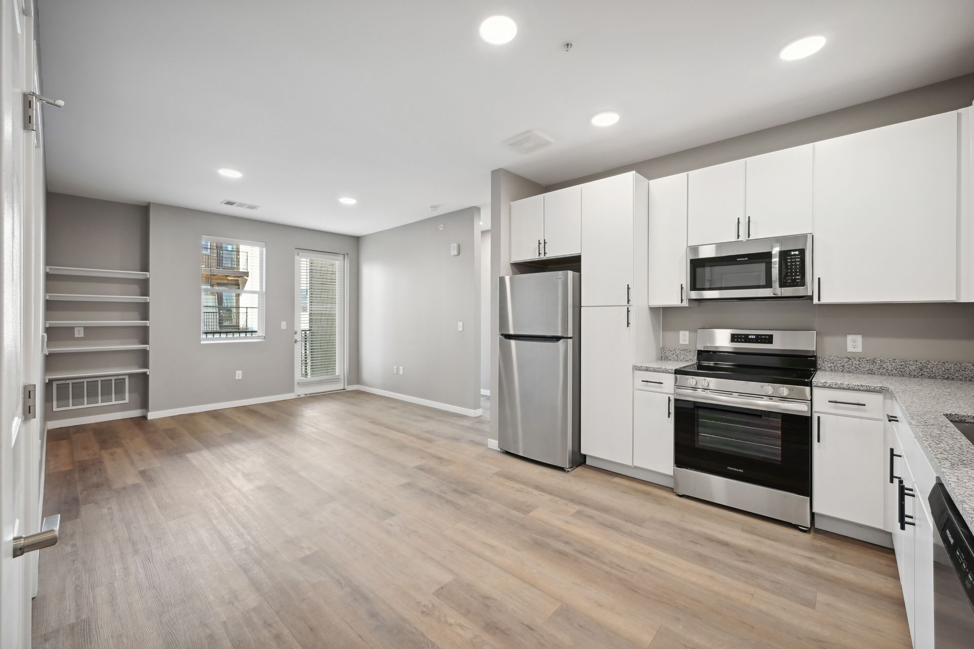 A modern, open-concept kitchen with white cabinets, stainless steel appliances, and light wood flooring in a living area.