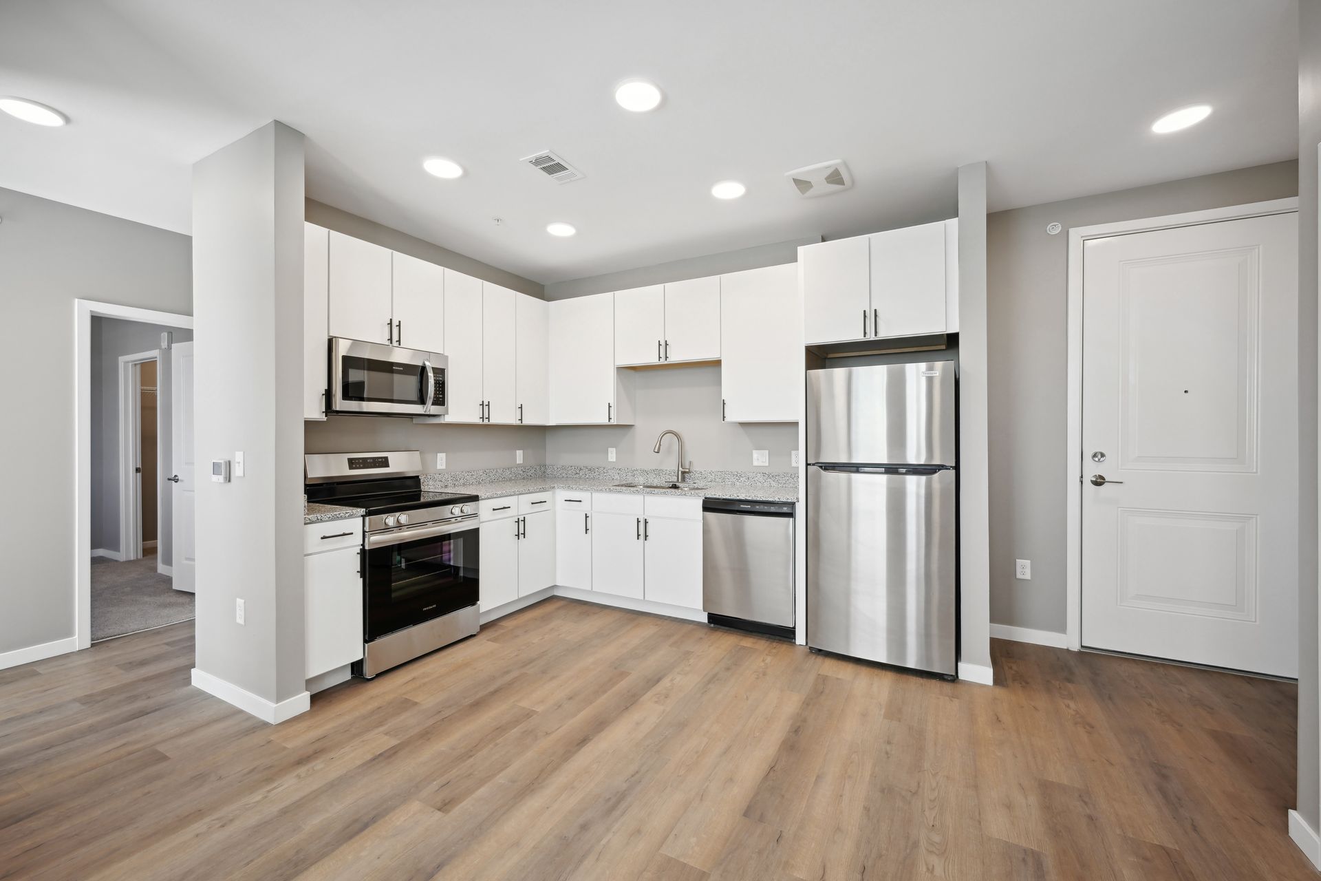 Modern kitchen with white cabinets, stainless steel appliances, light wood floors, and gray walls.