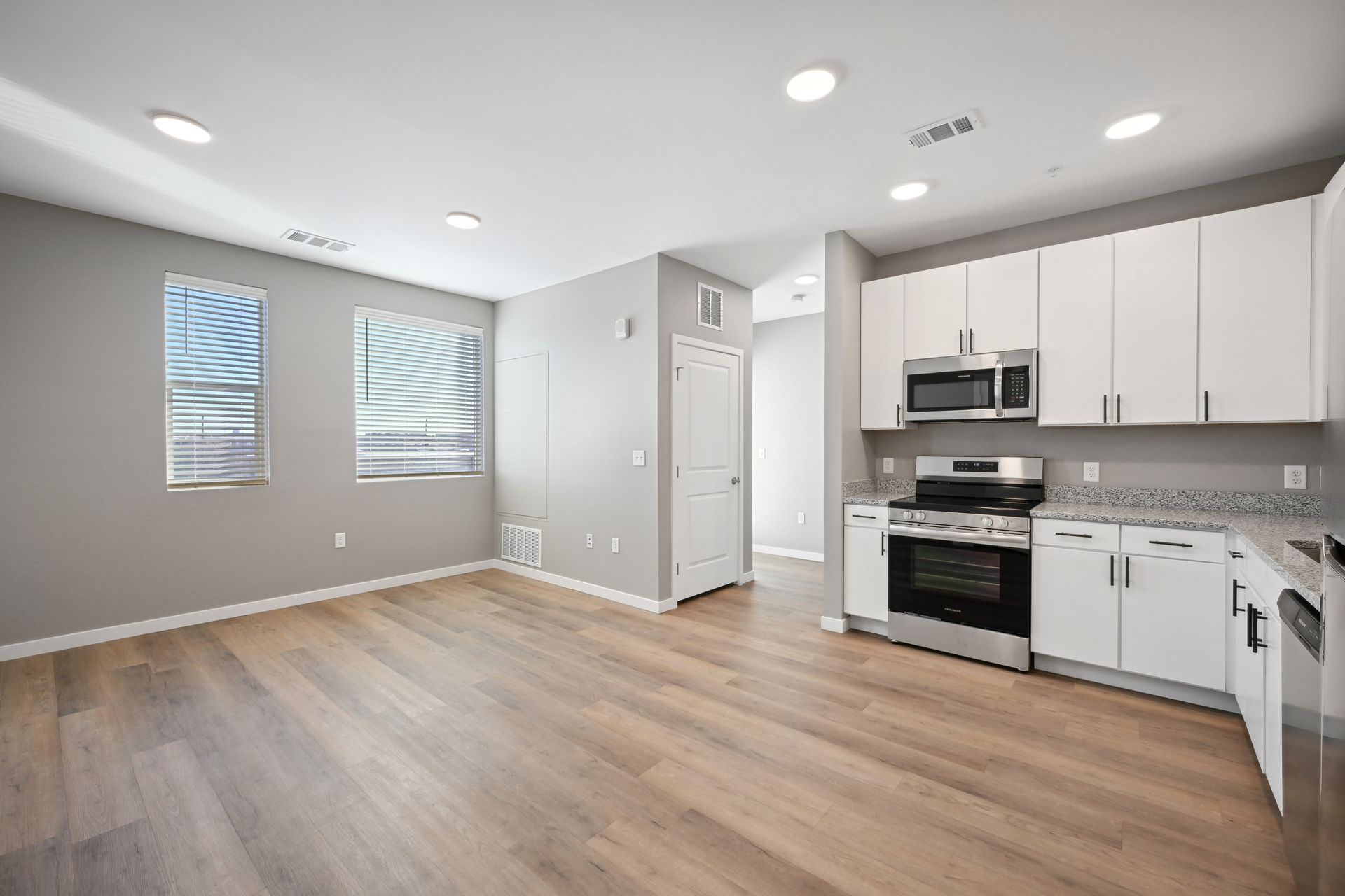 Modern kitchen and living area with grey walls, light wood floors, and white cabinets.