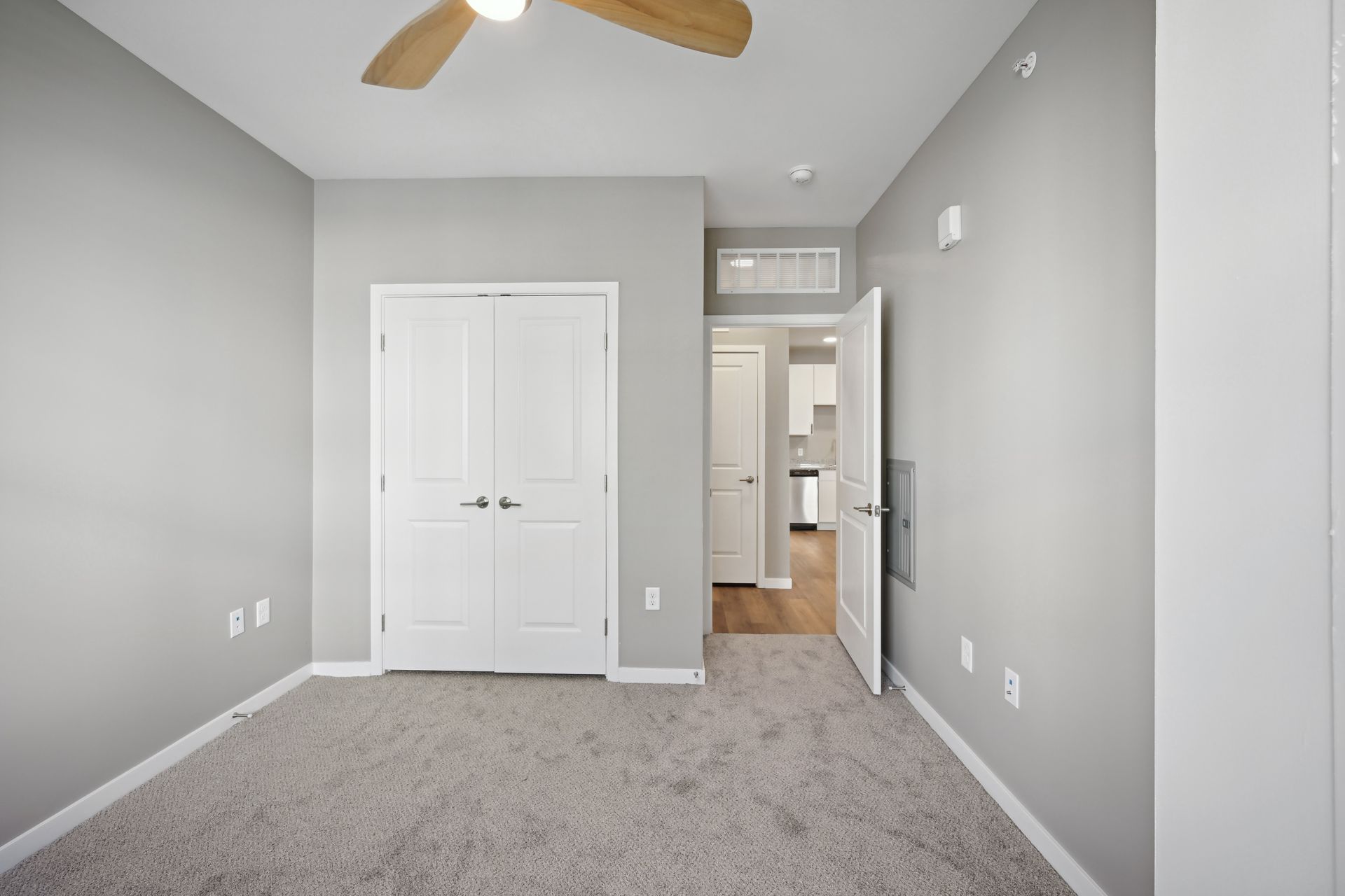 An unfurnished room with light gray walls, gray carpet, a white closet, and an open doorway leading to a hallway.