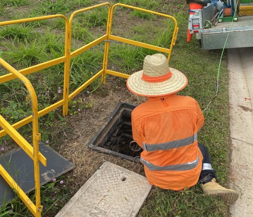 A Man Wearing a Straw Hat is Kneeling Down Next to a Manhole — Adzcom Civils in Portsmith, QLD