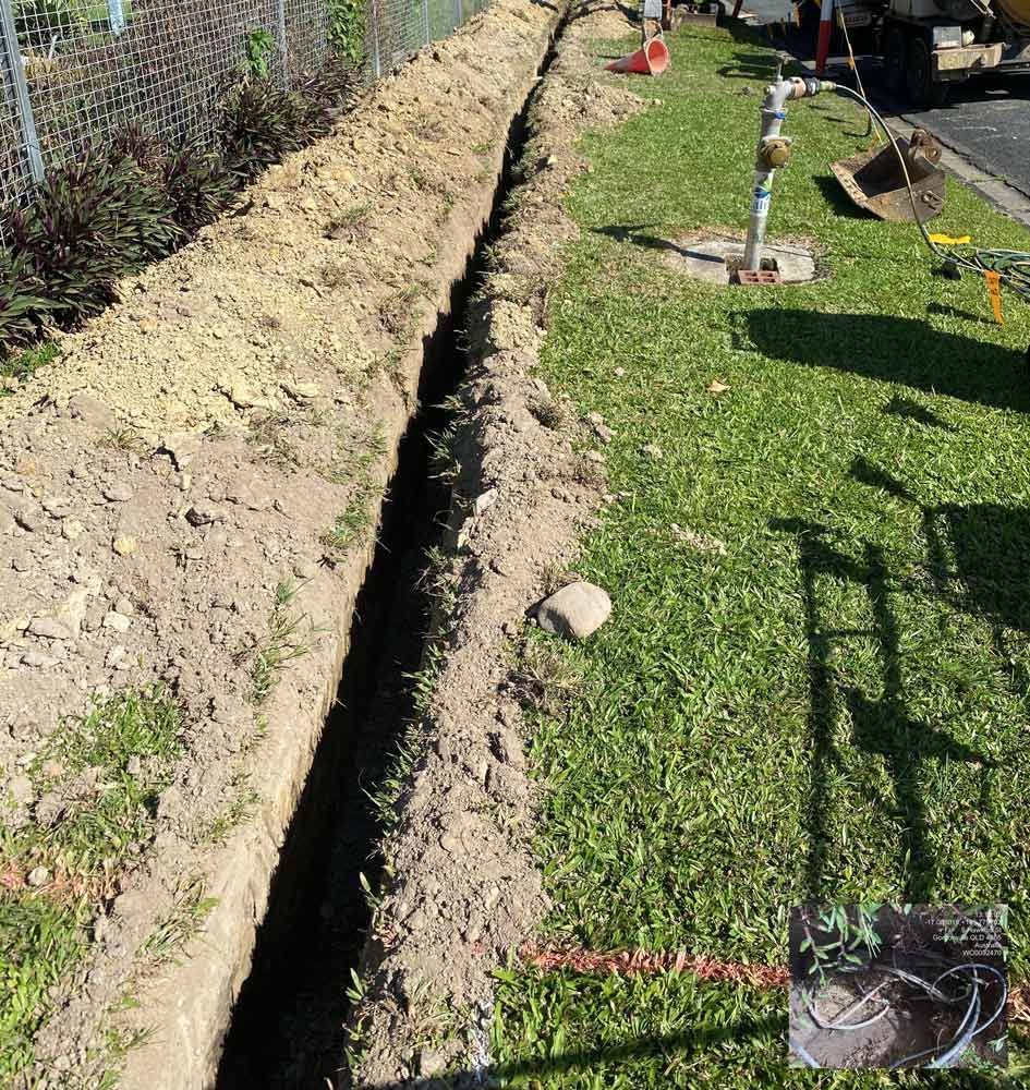 A Trench is Being Dug in the Grass Next to a Fence — Adzcom Civils in Port Douglas, QLD
