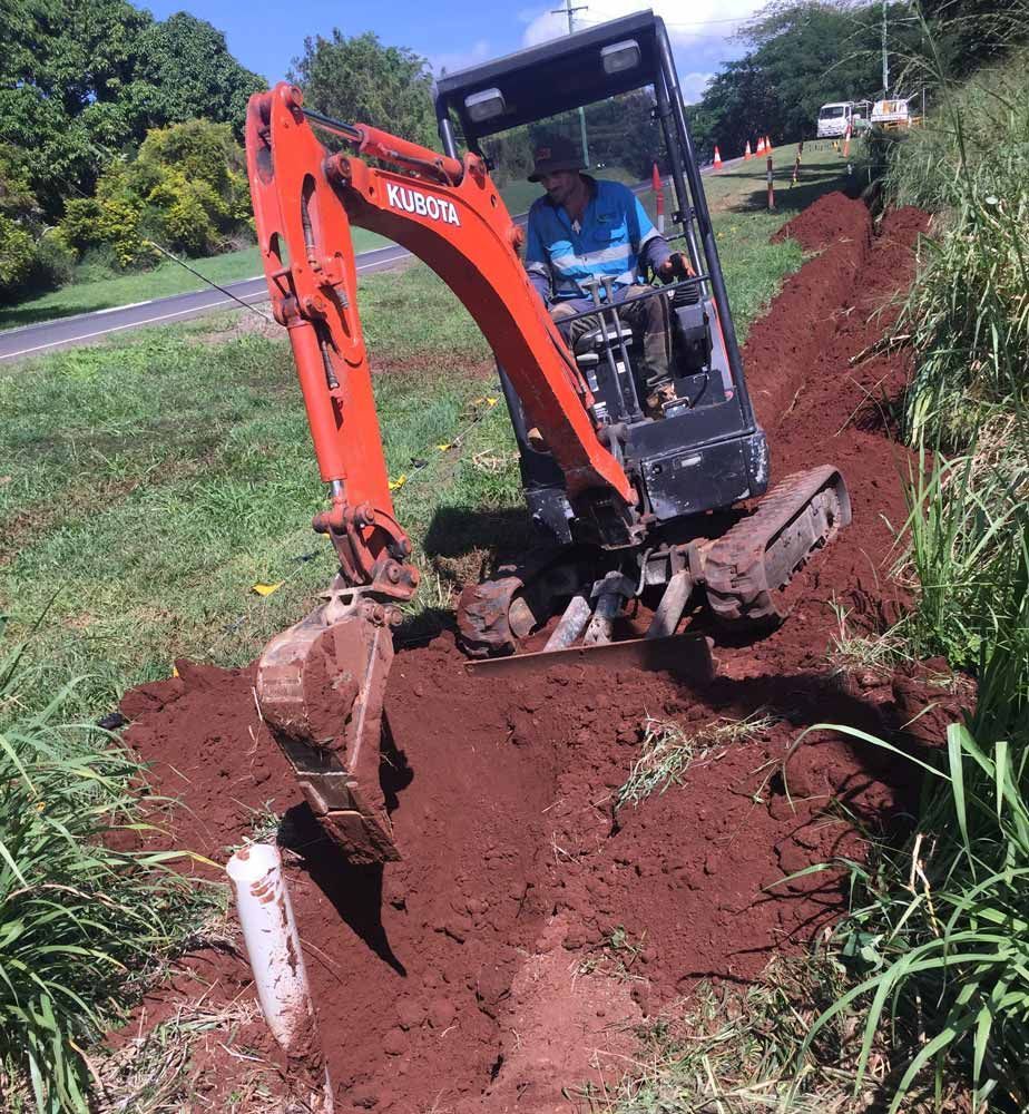 A Man is Driving a Kubota Excavator on a Dirt Road — Adzcom Civils in Portsmith, QLD