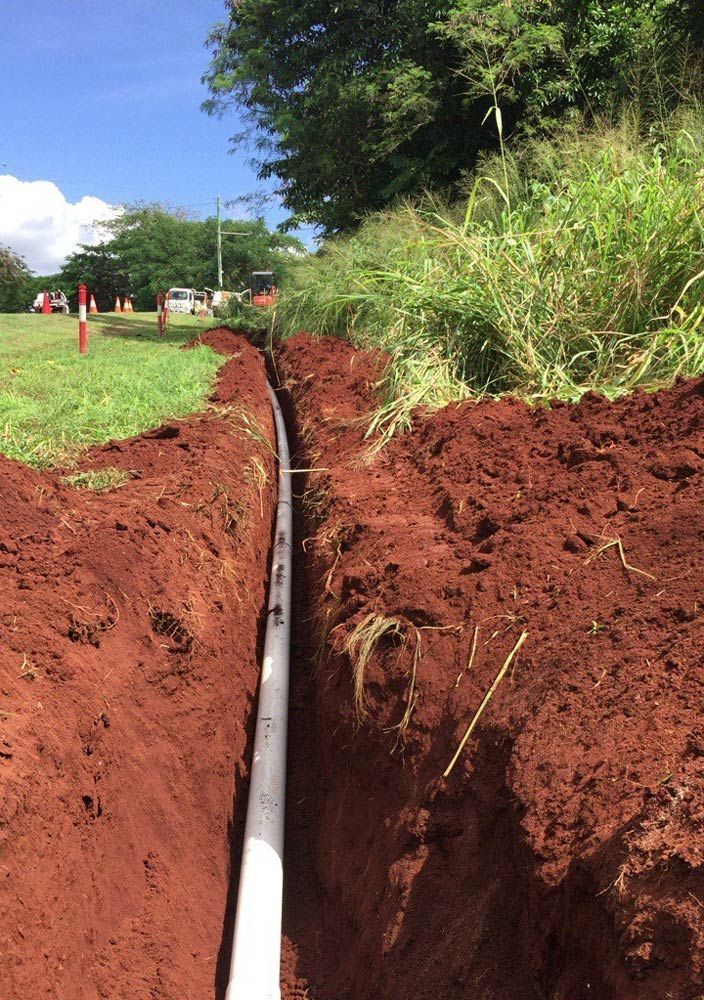 A Pipe is Being Installed in the Dirt Next to a Grassy Field — Adzcom Civils in Portsmith, QLD