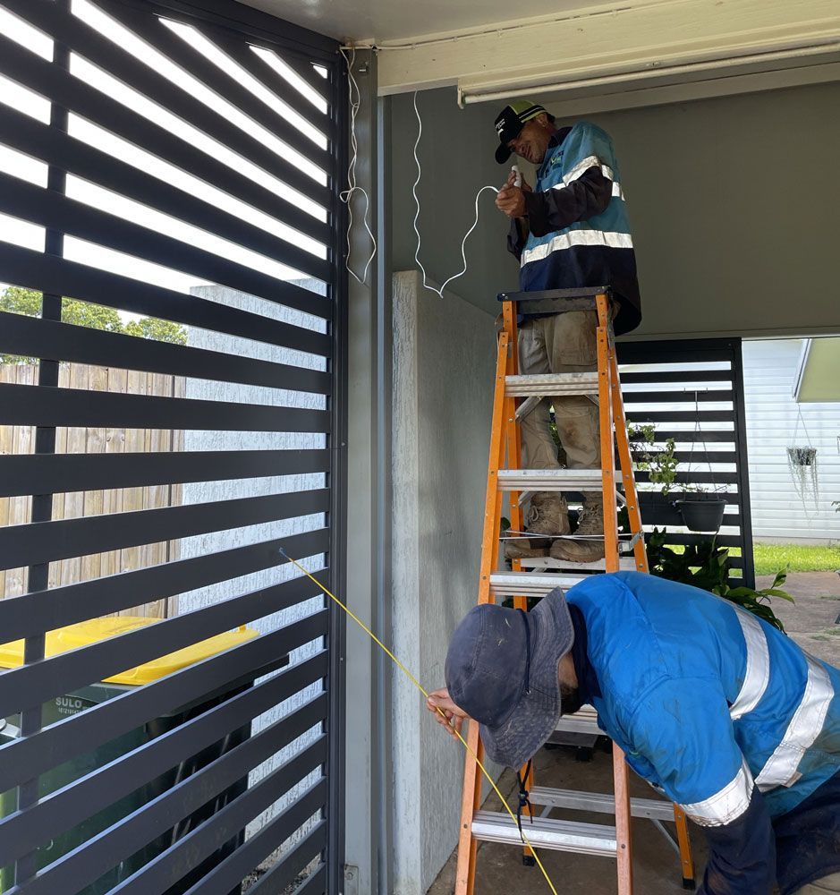 A Man on a Ladder Measuring a Fence With a Tape Measure — Adzcom Civils in Innisfail, QLD