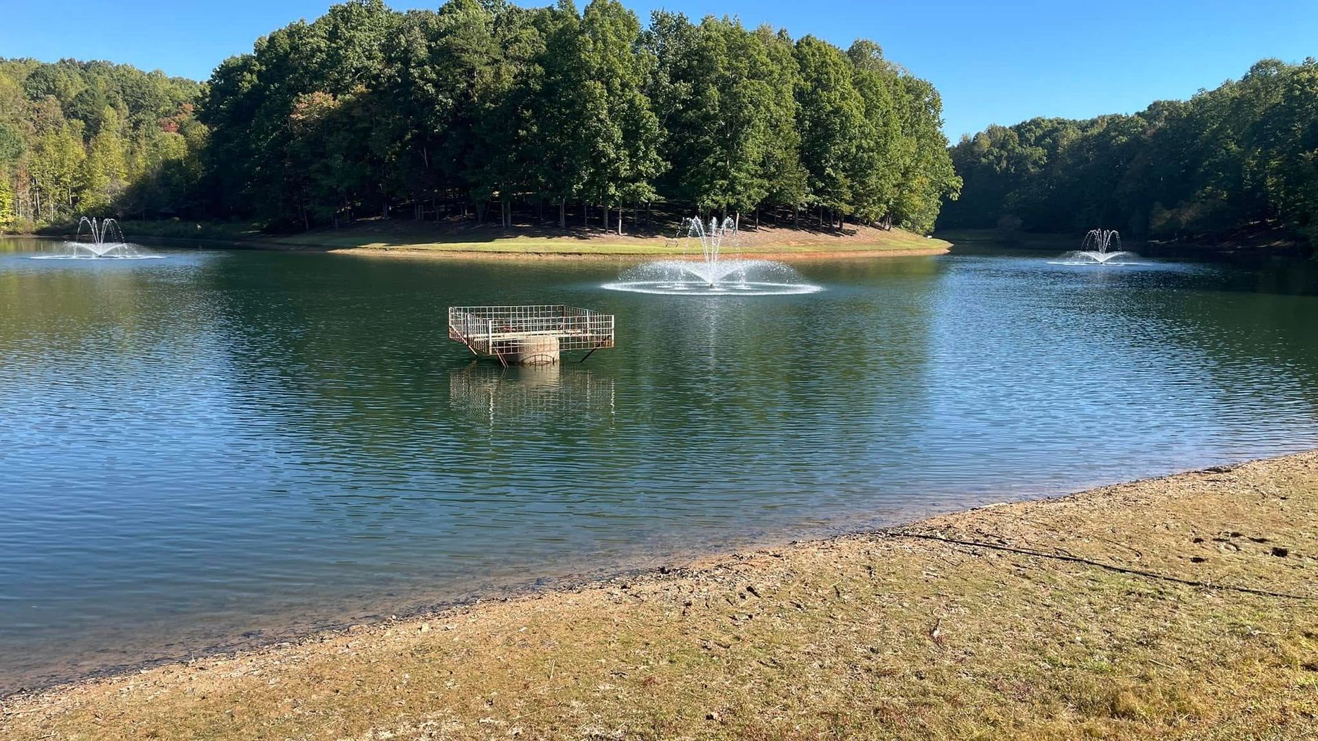 Lake scene with fountains, trees, and a small, brown shoreline.
