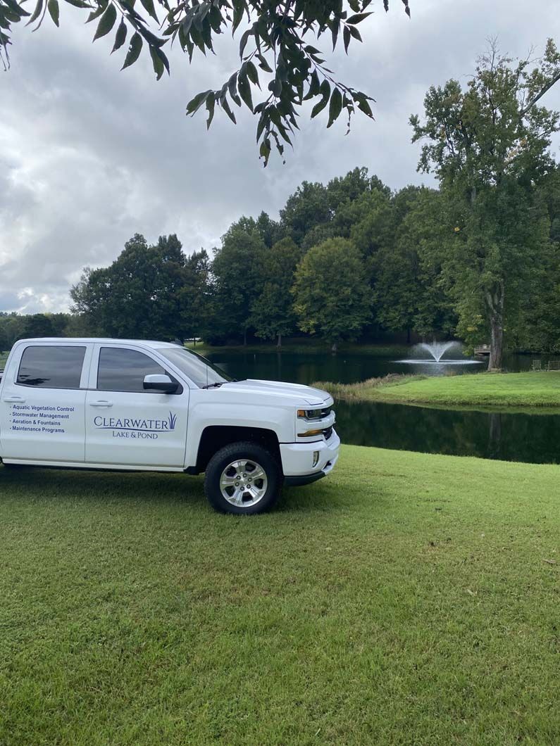 White truck parked on a grassy lawn, overlooking a pond with a fountain, under a cloudy sky.