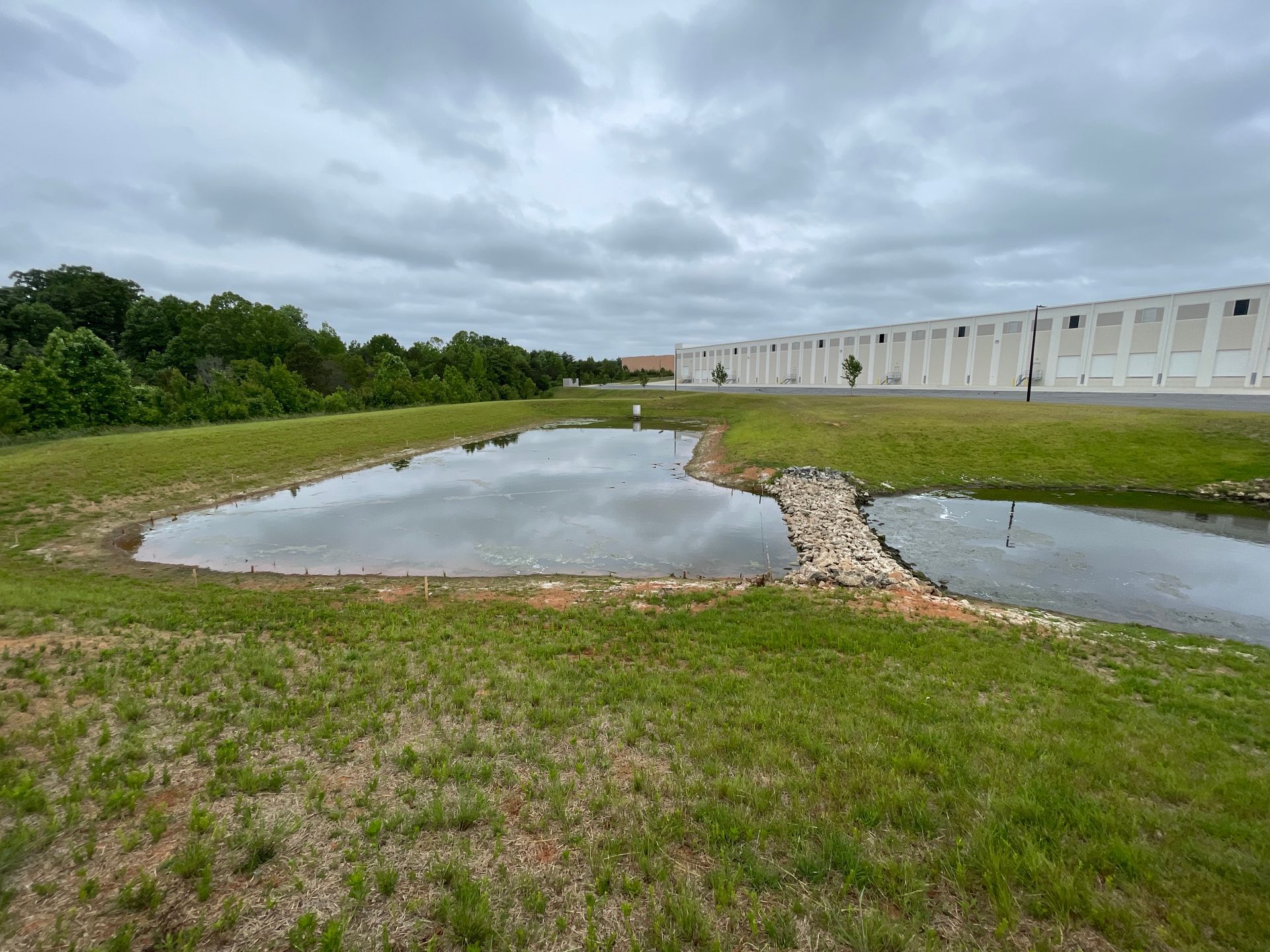 Grassy area with ponds and trees near a white building under a cloudy sky.
