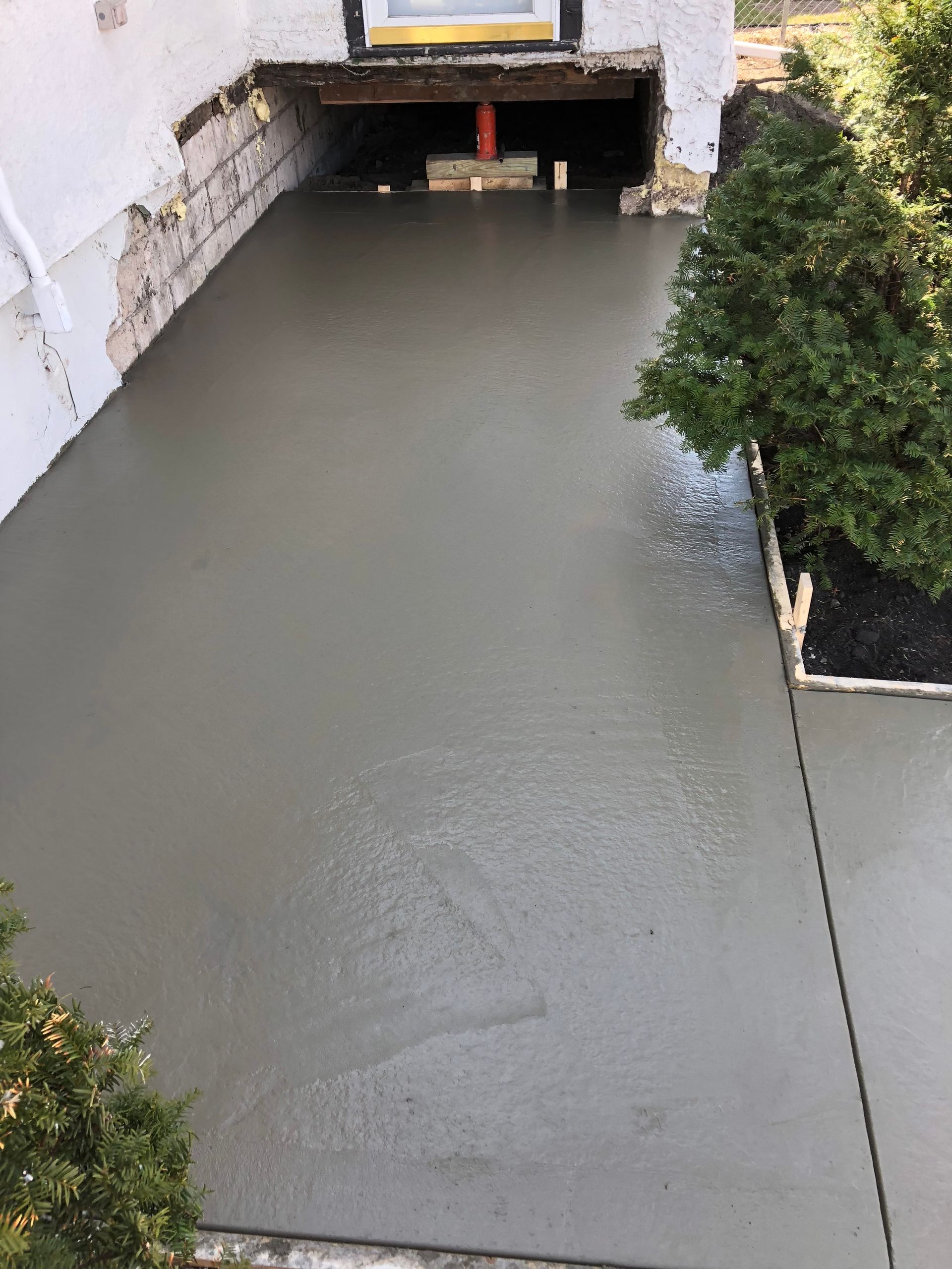 A freshly poured, smooth gray concrete walkway leads to an entryway with a visible support post underneath the porch.