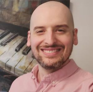 A bald man with a beard is smiling in front of a piano.