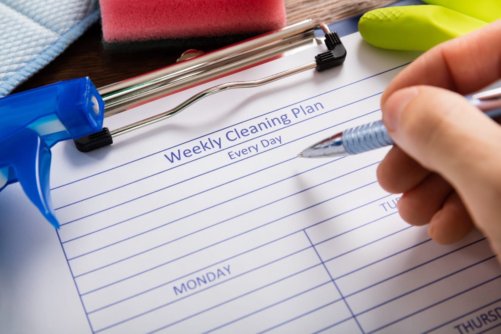 A person is writing on a weekly cleaning plan with a pen.
