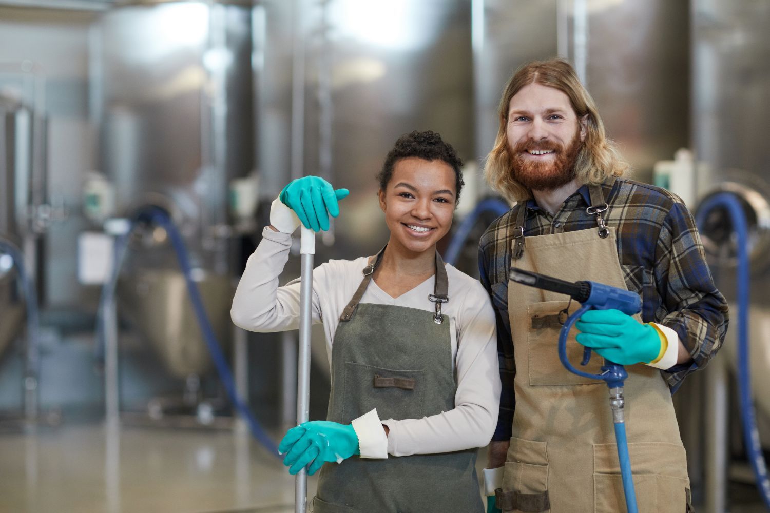 A man and a woman are standing next to each other in a factory holding cleaning supplies.