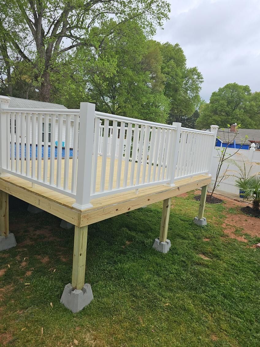 A wooden deck with a white railing is sitting on top of a lush green field.