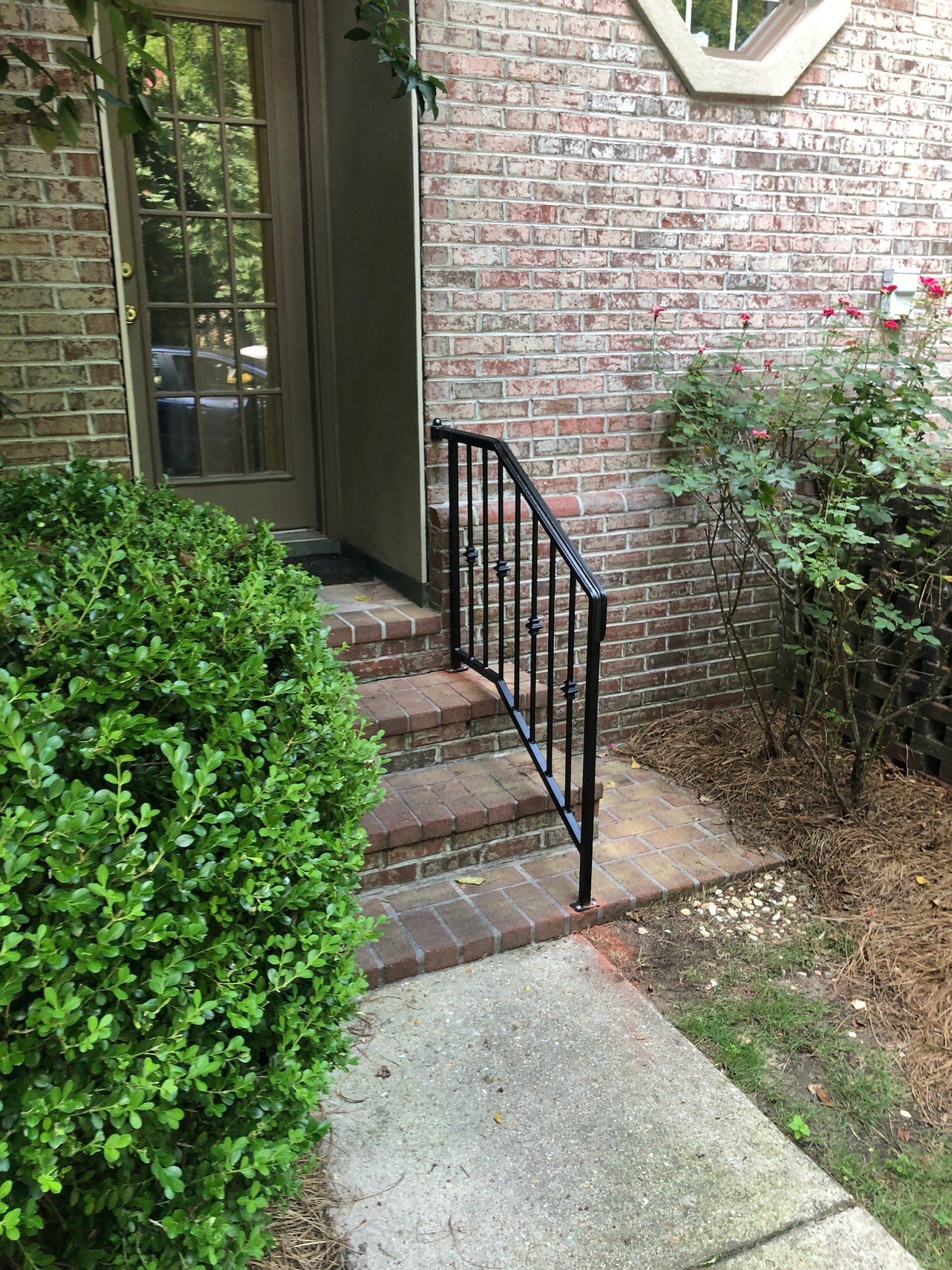 a wrought iron railing is attached to the sidewalk in front of a brick house .