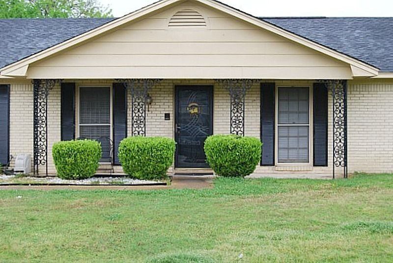 a brick house with black shutters and bushes in front of it