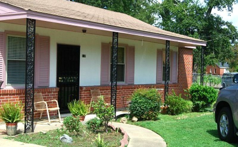 a brick house with pink shutters and a car parked in front of it