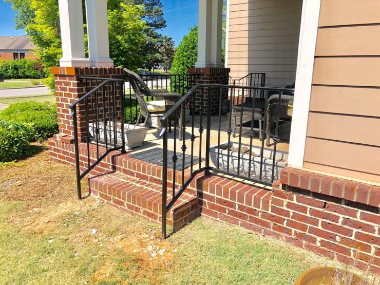 a brick porch with a wrought iron railing and steps leading to it .