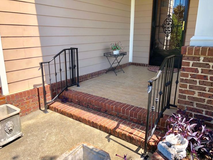 a brick porch with a metal railing and steps leading to it .