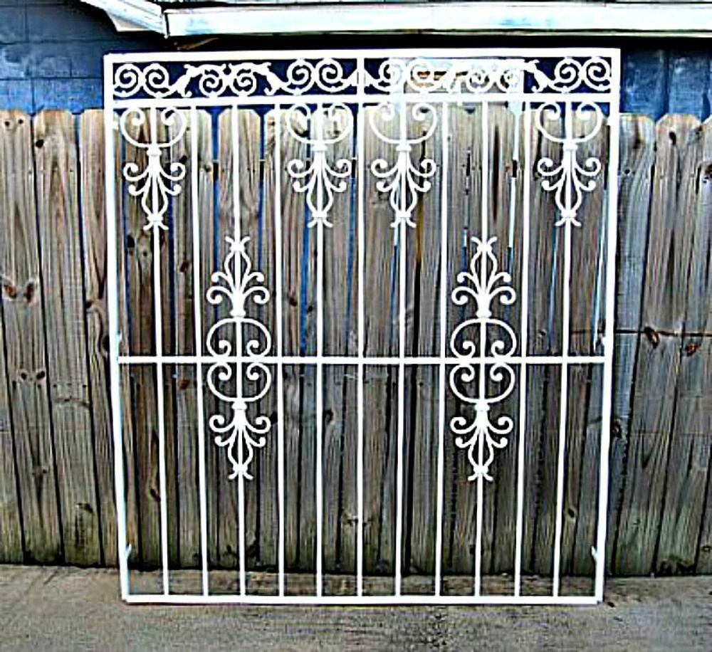 a white wrought iron gate is sitting in front of a wooden fence .