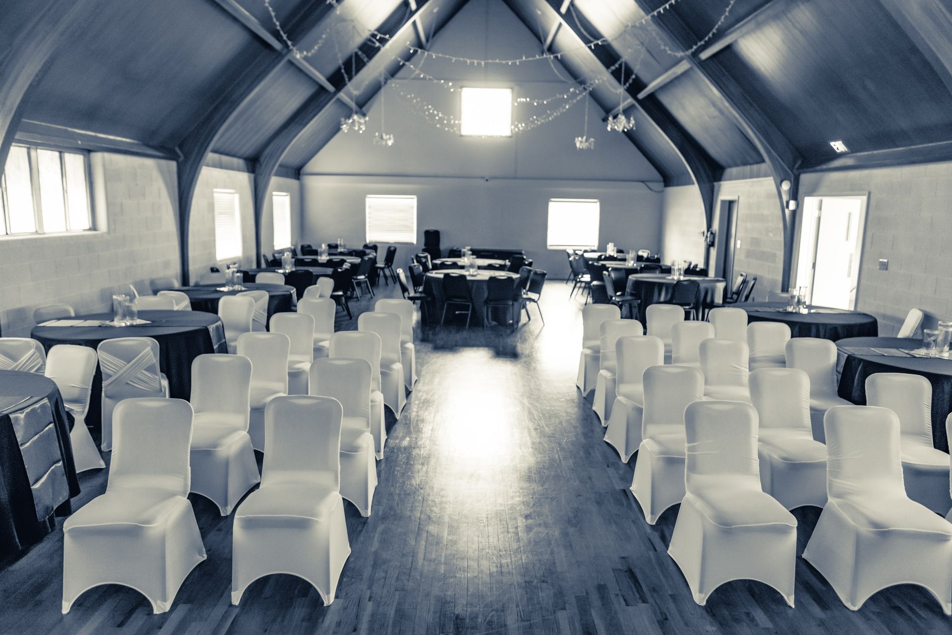 Empty hall set up for an event, chairs face a raised platform, tables in the background.