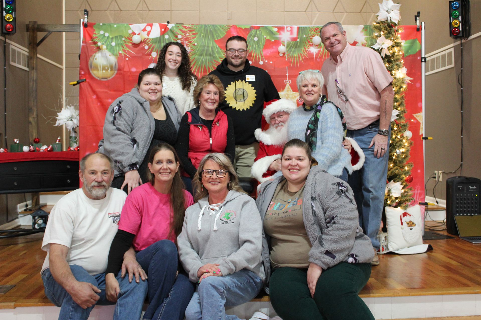 Group of people posing with Santa in front of a holiday backdrop.