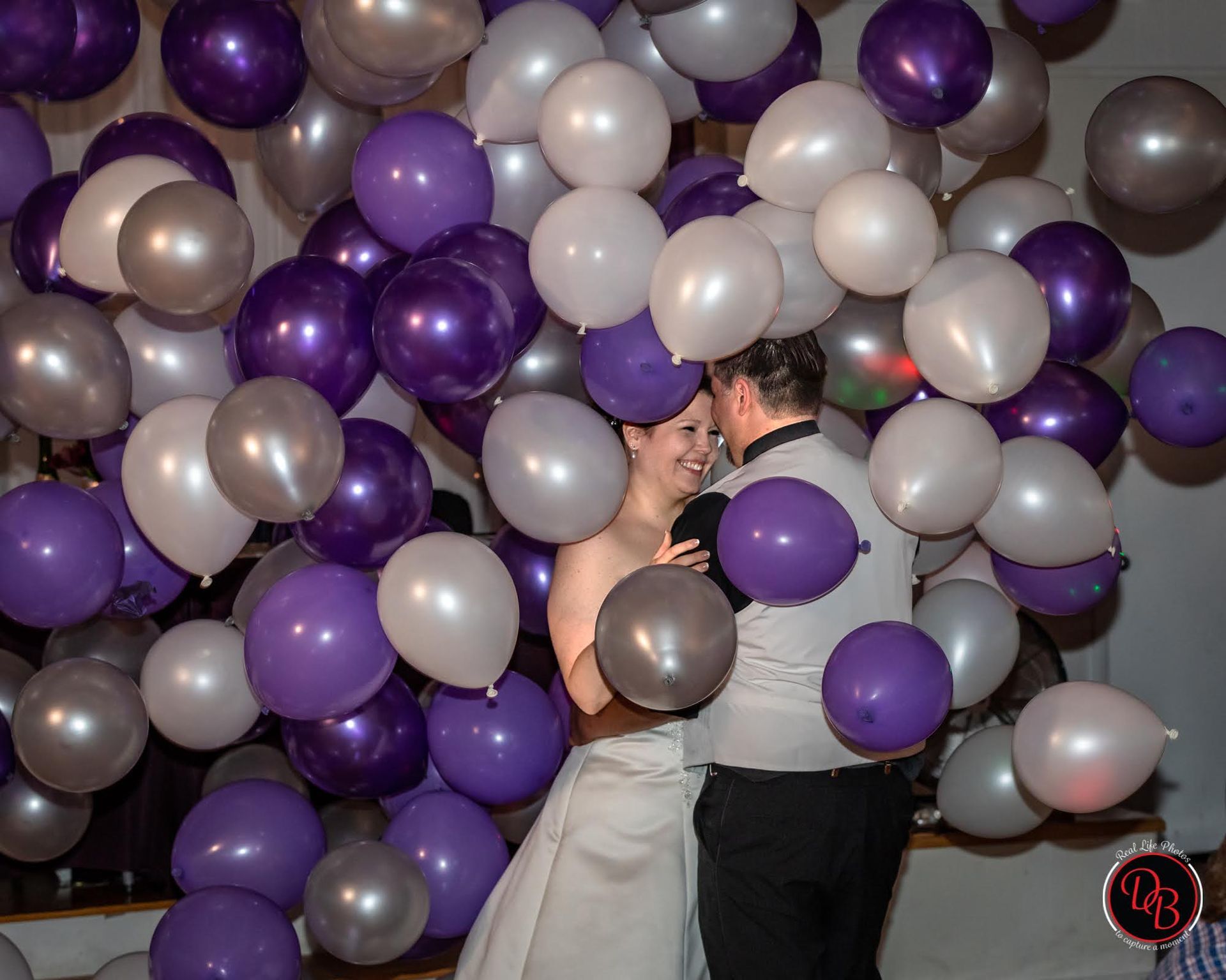 Newlyweds dance amid a backdrop of purple, silver, and white balloons.