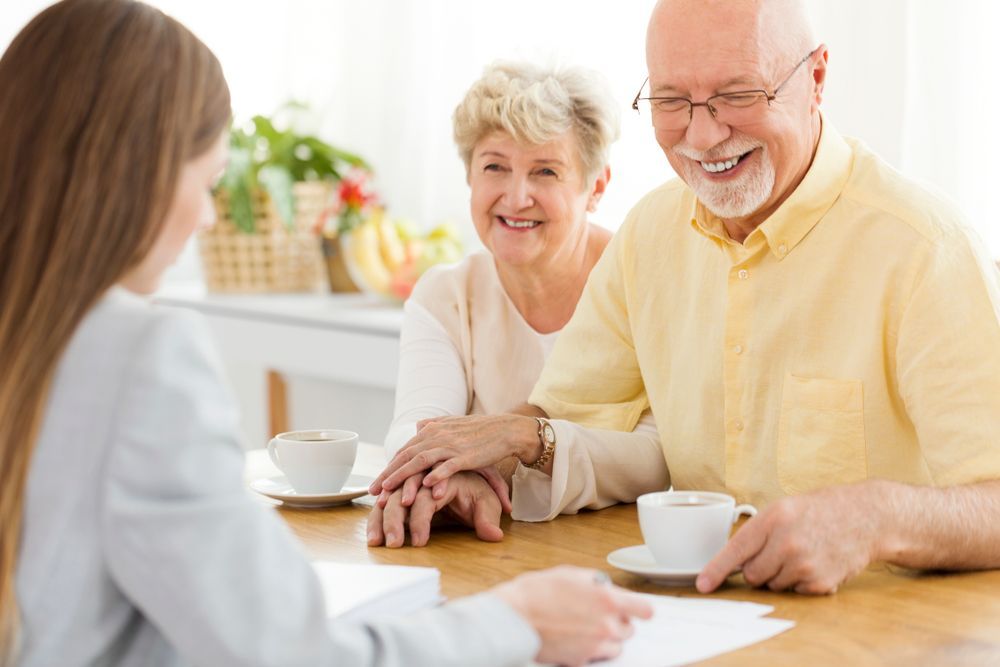 Woman in suit consults with smiling older couple at a table; they hold hands and have coffee.
