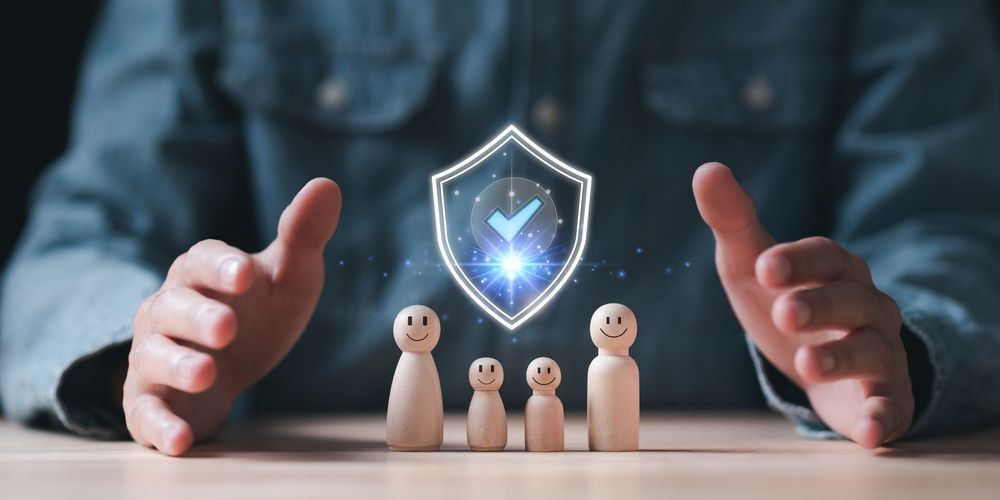Hands protecting wooden family figures under a glowing shield with a checkmark.