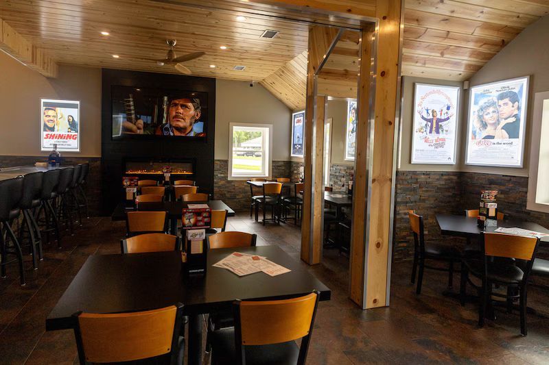 Restaurant interior with tables, chairs, bar, and movie posters; a television is on the wall.