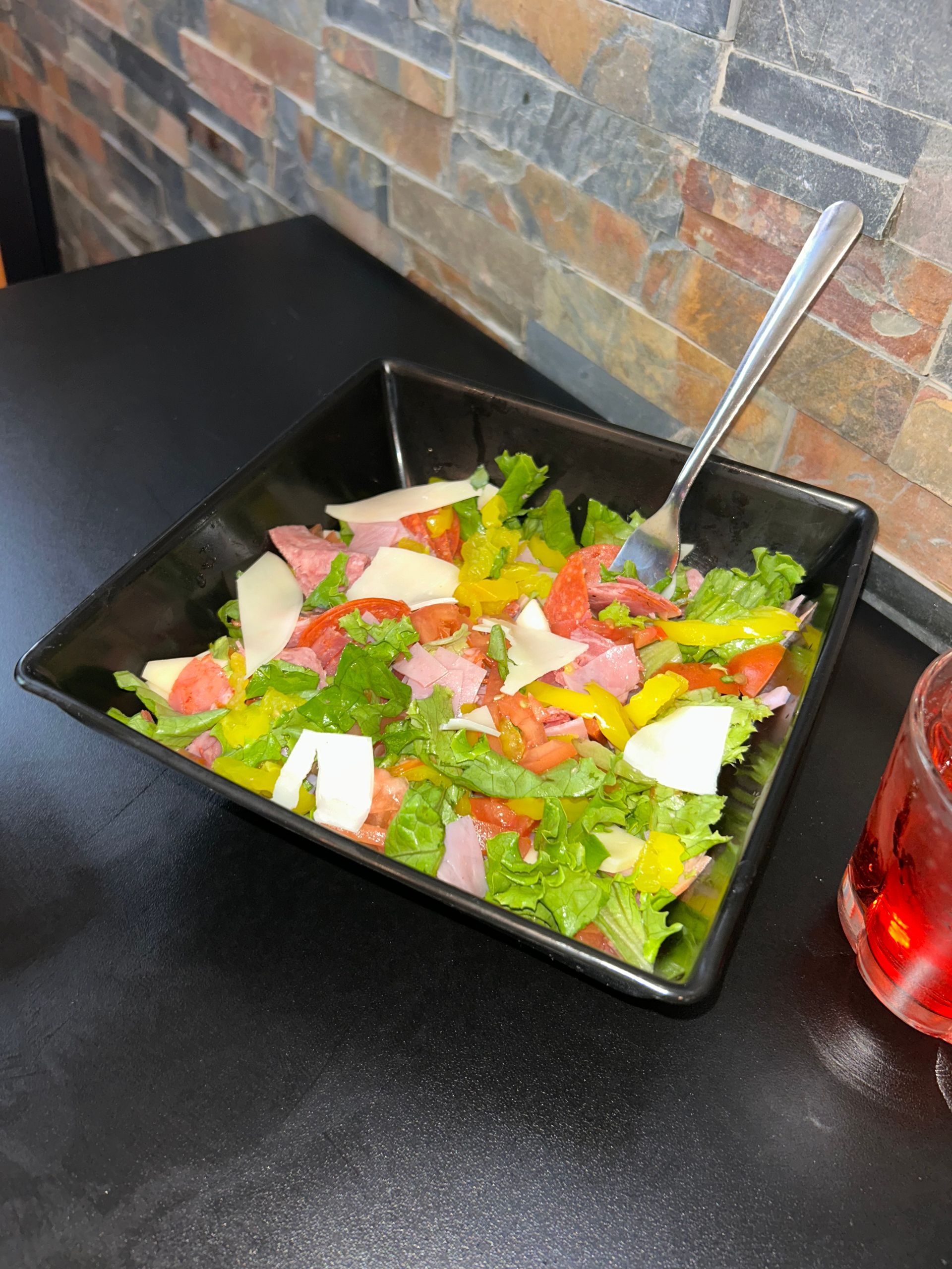 Salad with lettuce, tomatoes, peppers, and cheese in a black bowl, on a black table with a fork.