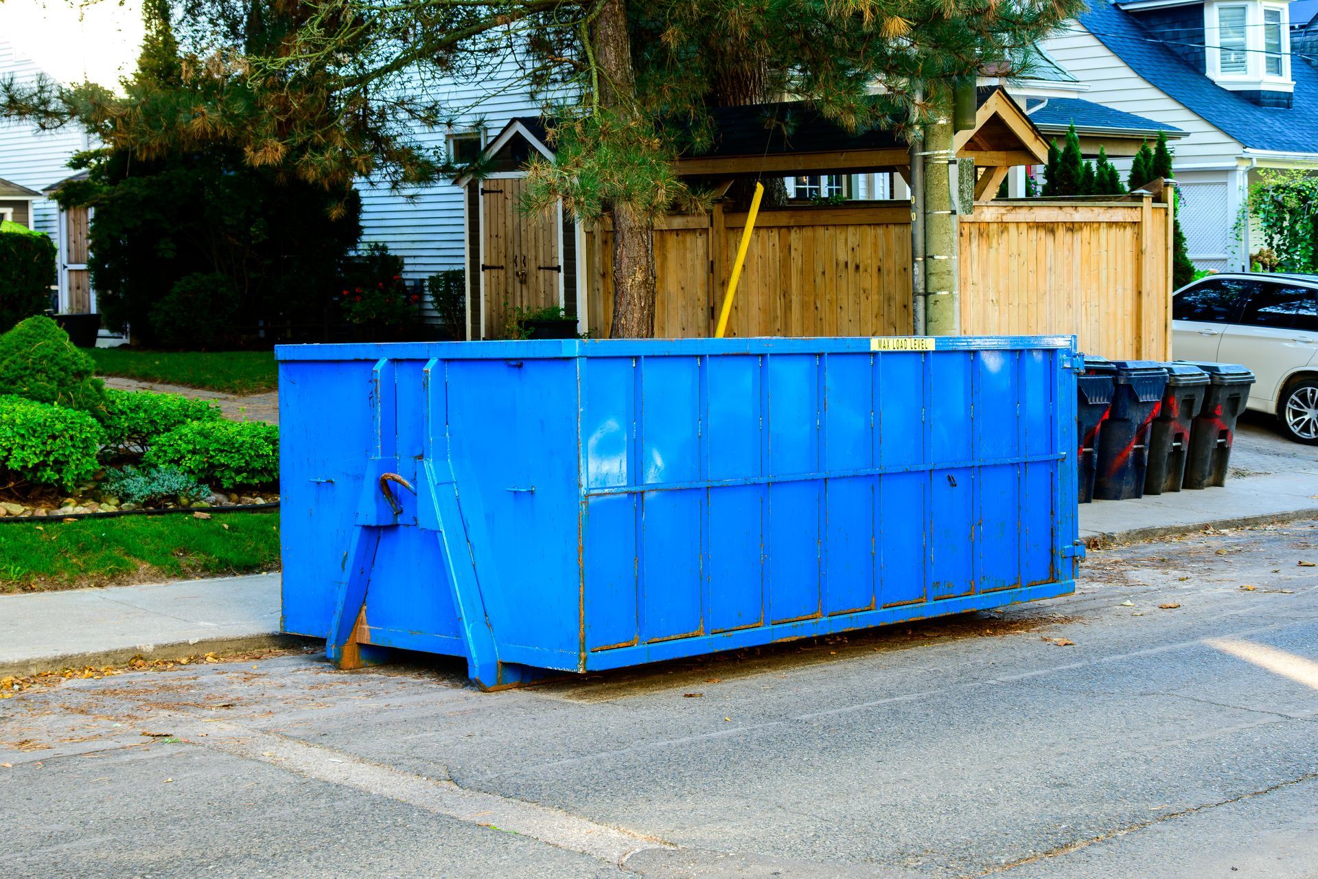 A blue dumpster is parked on the side of the road in front of a house.