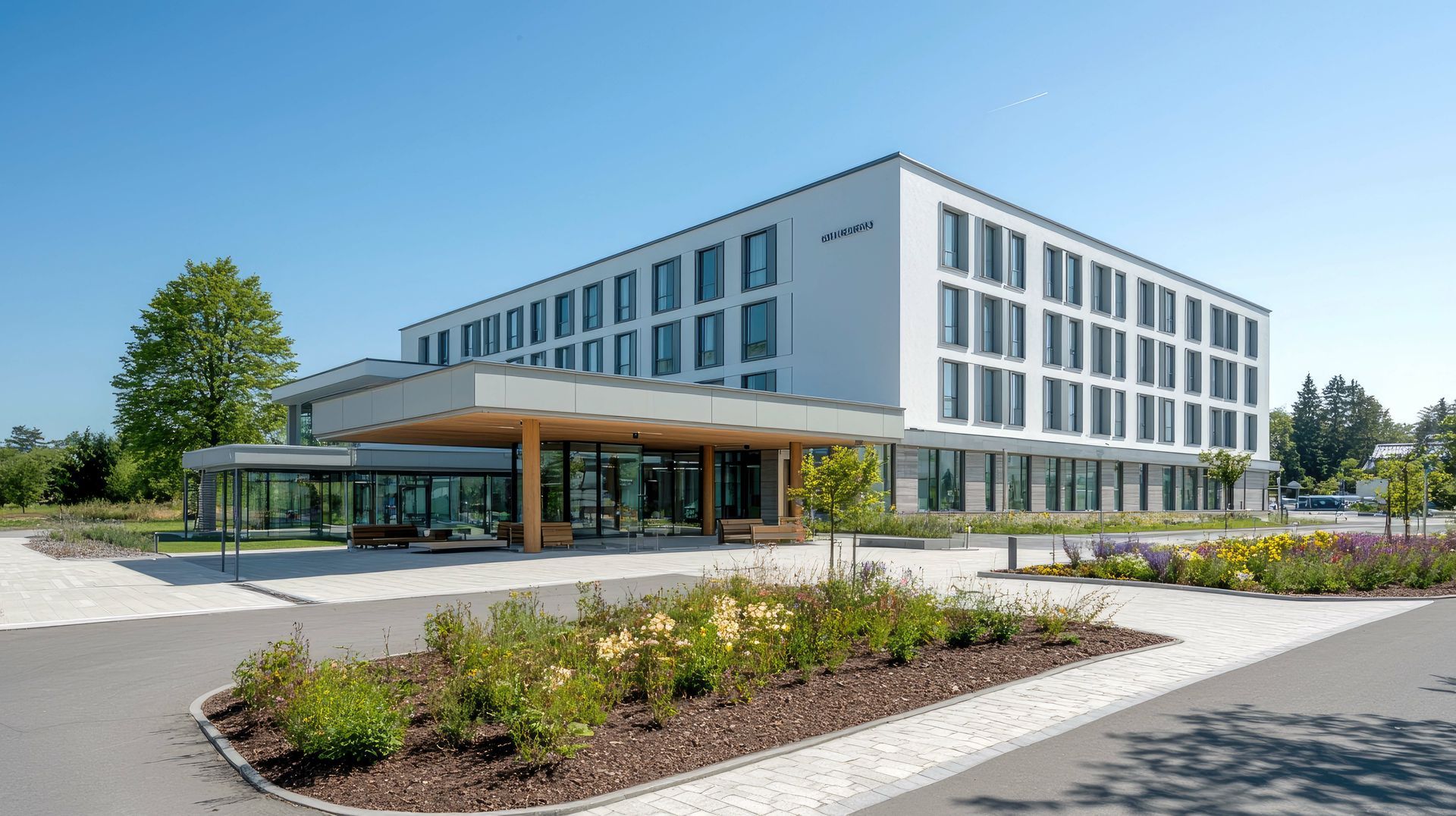 A large white building with a lot of windows is surrounded by trees and bushes.