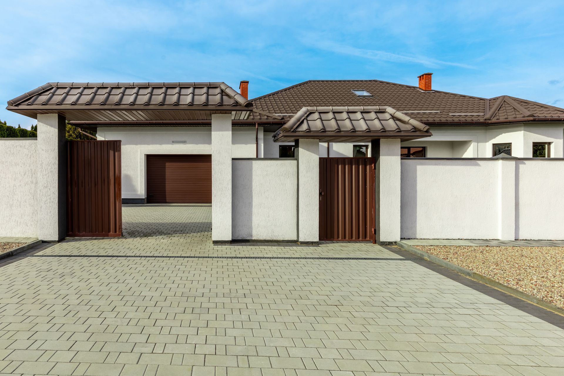 A white house with a brown roof and a driveway leading to it.