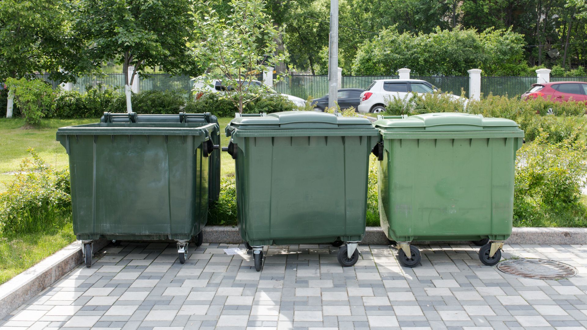 Three green garbage cans are parked next to each other on a sidewalk.