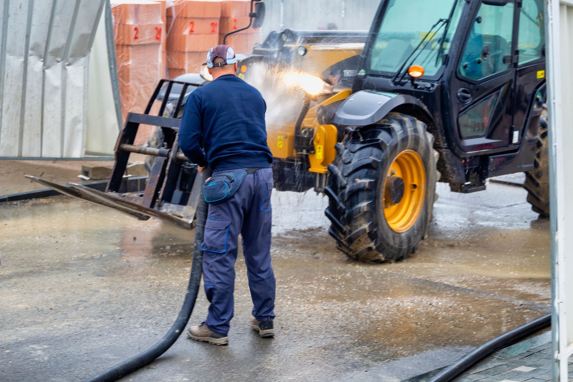 A man is washing a tractor with a hose.