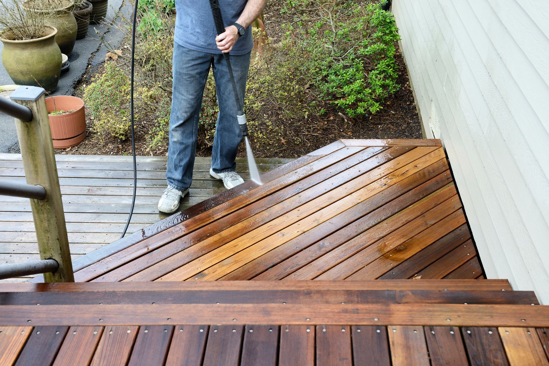 A man is cleaning a wooden deck with a high pressure washer.